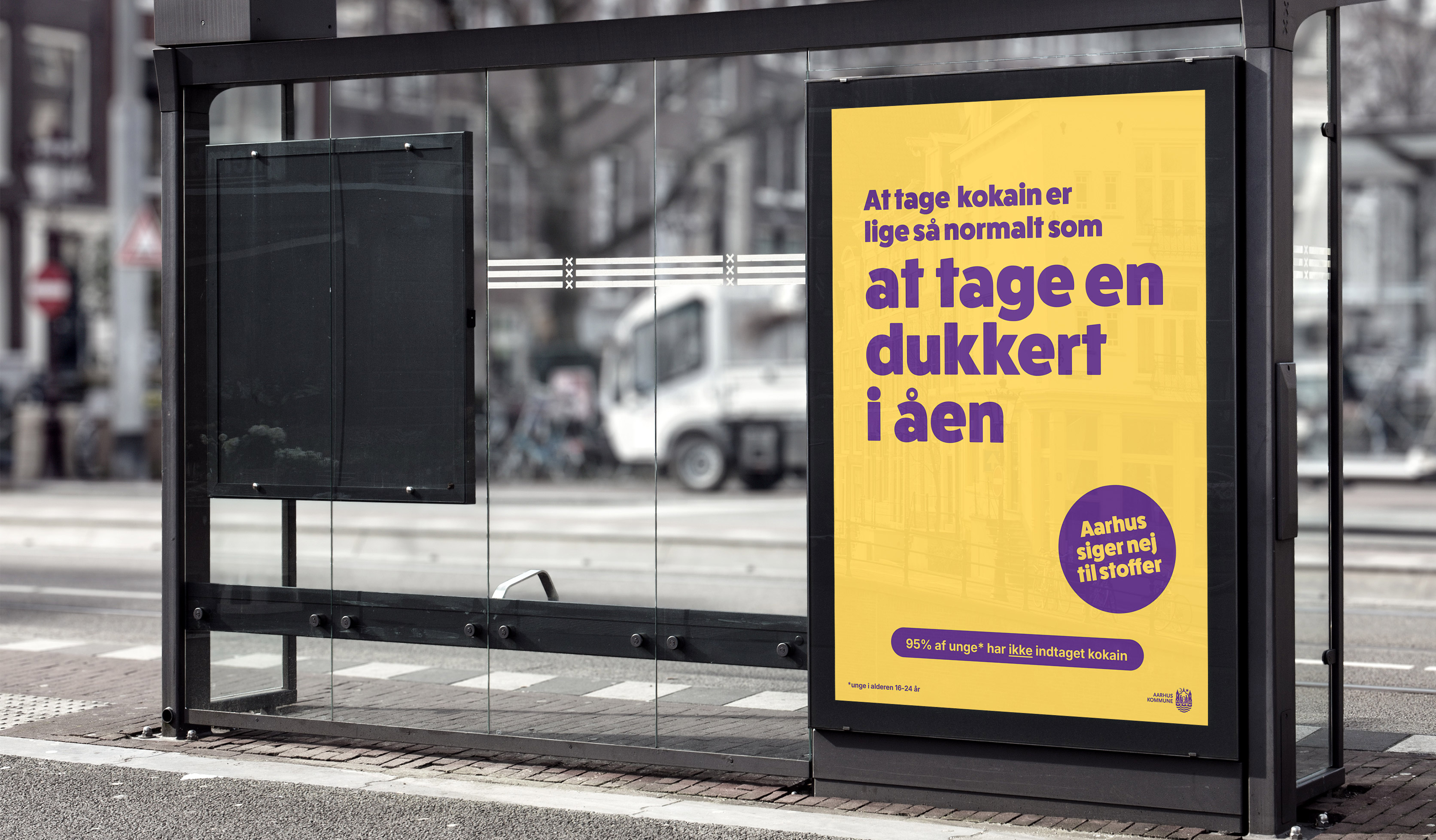 Billede af en busstation med en plakat hvorpå, der står: At tage kokain er ligeså normalt som at tage en dukkert i åen. Aarhus siger nej til stoffer. 95 % af unge i alderen 16-24 år har ikke indtaget kokain.